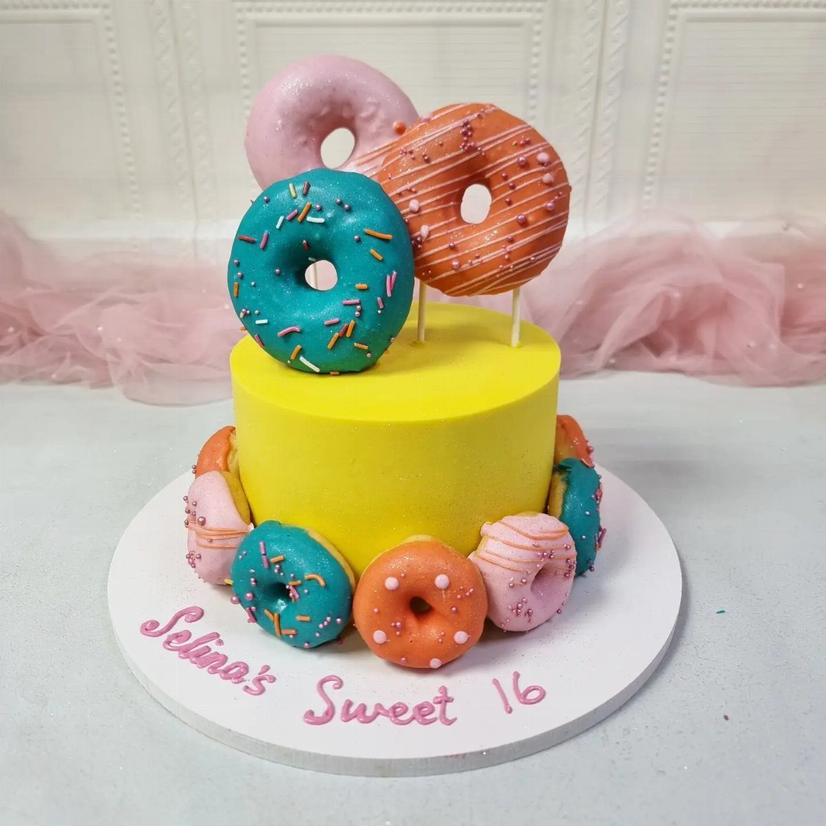 Yellow sweet 16 cake decorated with colorful frosted donuts and pink lettering.