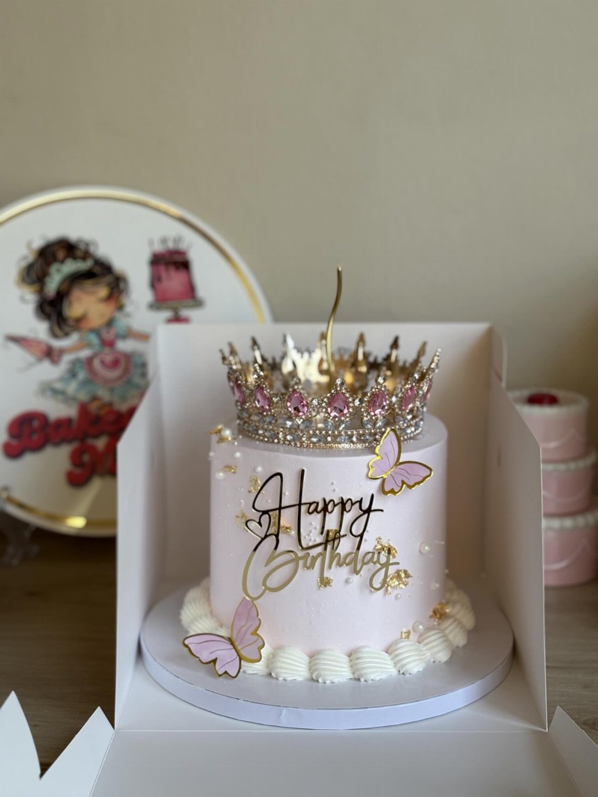 Light pink birthday cake topped with a golden tiara and pink butterflies.