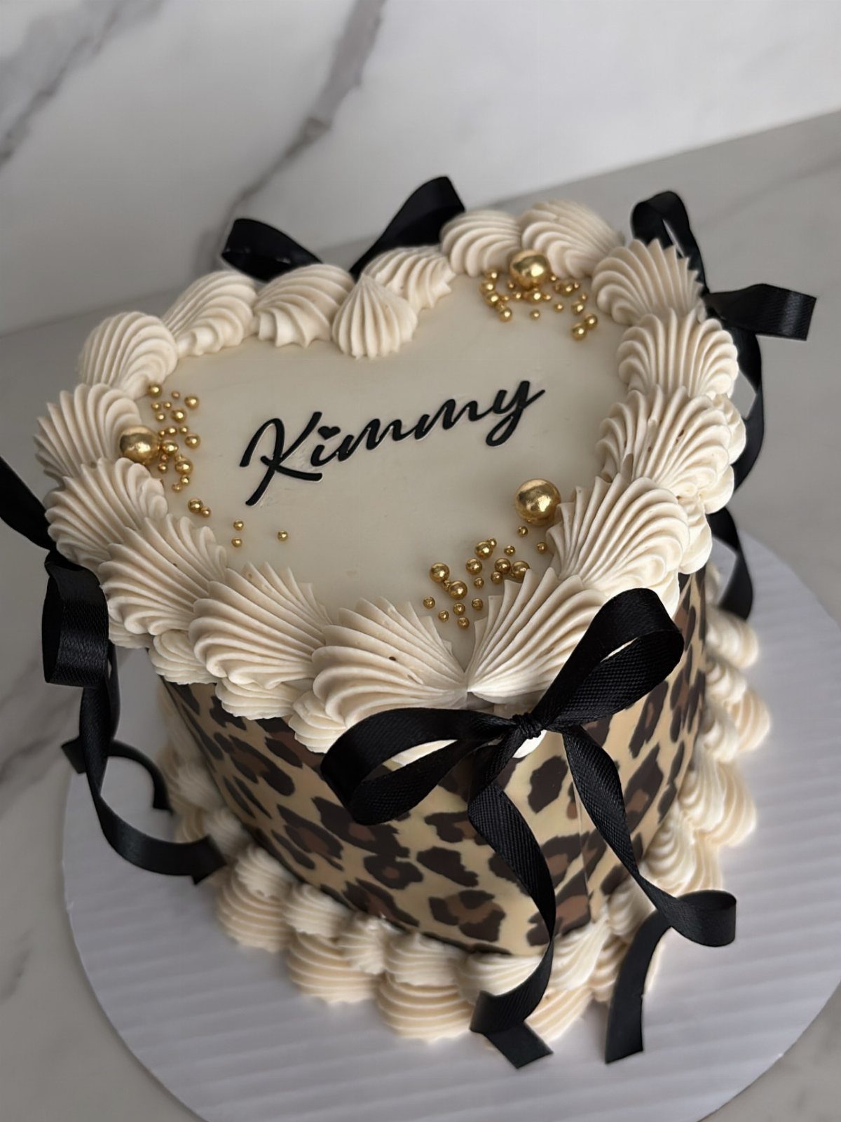 Heart-shaped cake with leopard print sides, white frosting, and black ribbon bows.