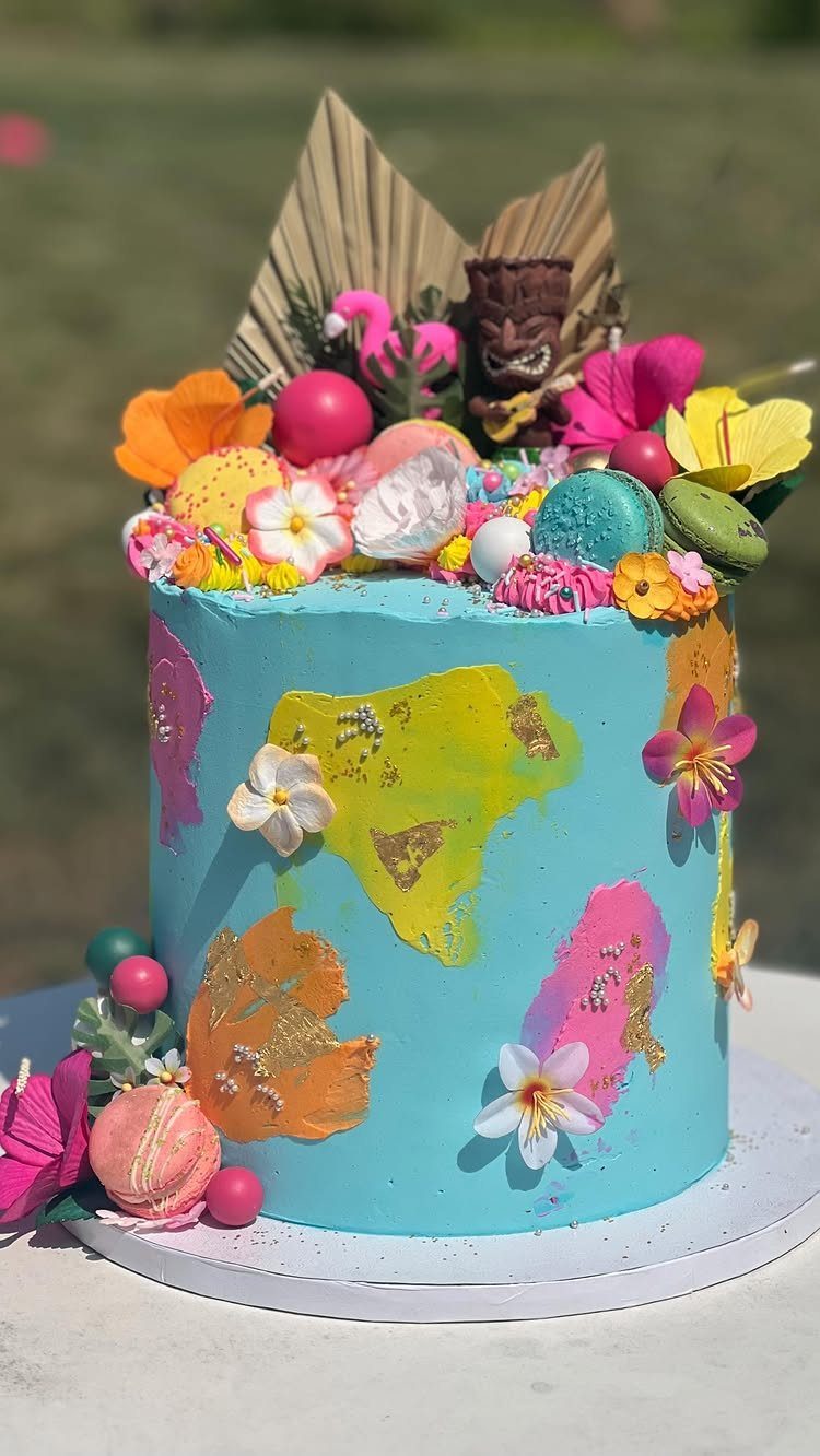 Light blue tropical cake topped with a tiki statue, macarons, and flowers.