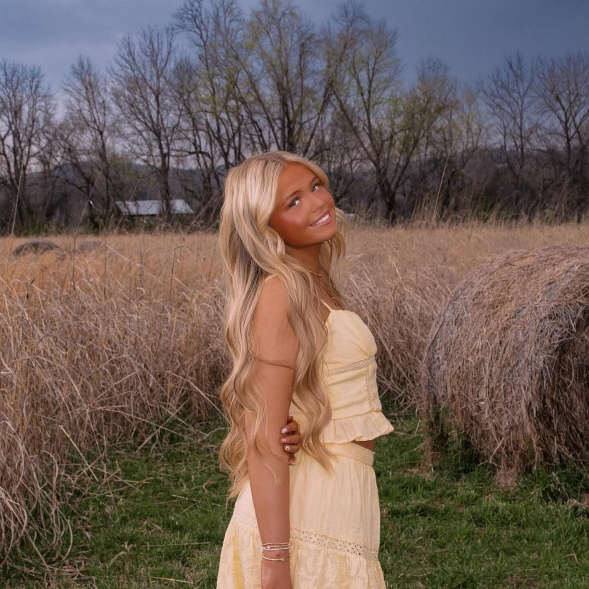 Young woman in a yellow tiered boho dress posing in a grassy field
