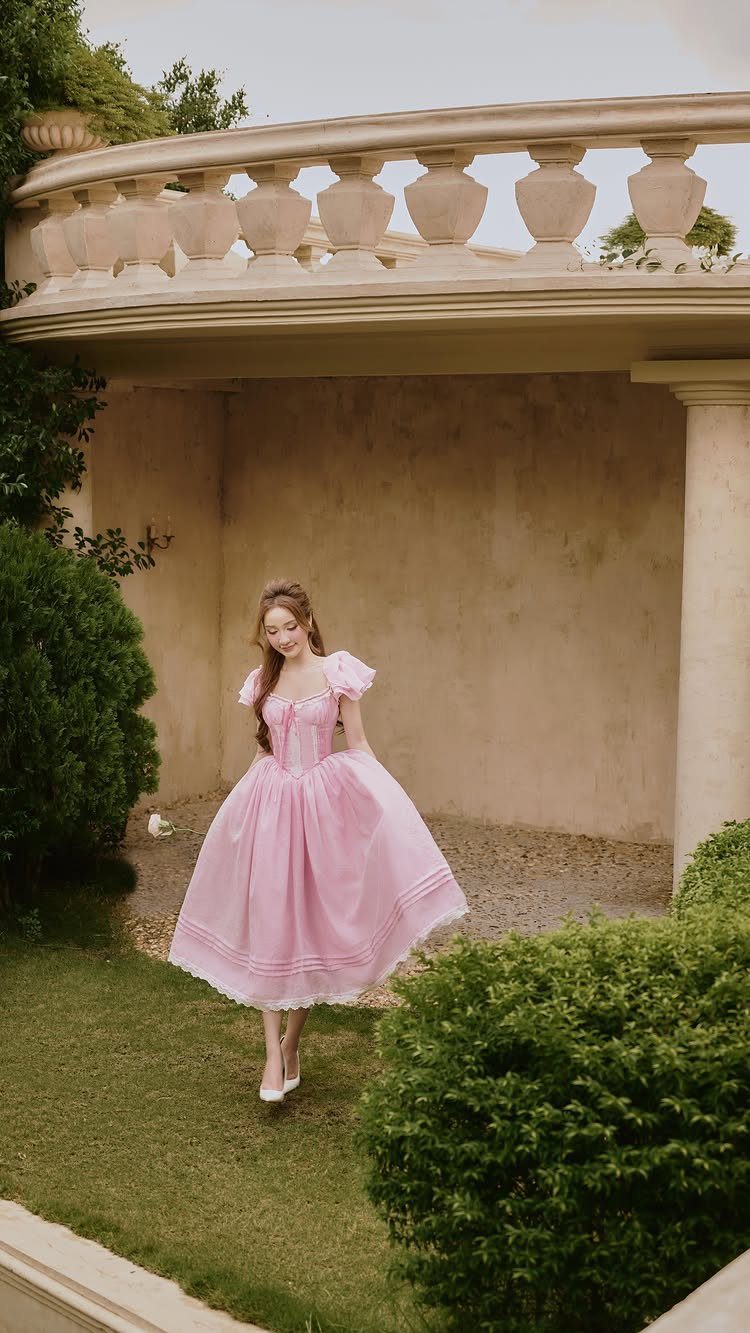 Young woman in a pink corset bodice dress standing in a stone courtyard.