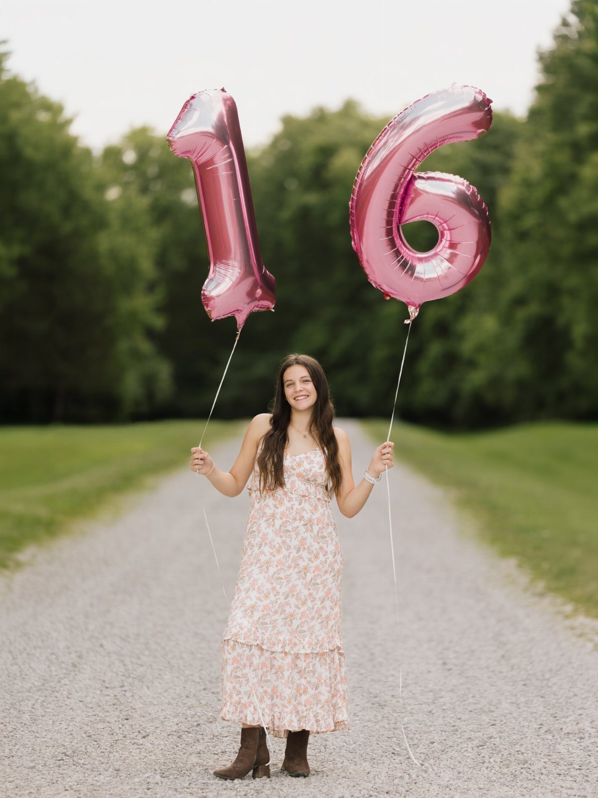 Teenage girl in a floral print maxi dress holding pink number 16 balloons.