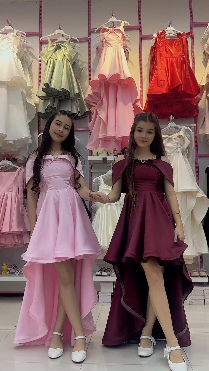 Two girls wearing high-low formal dresses in pink and burgundy in a boutique.