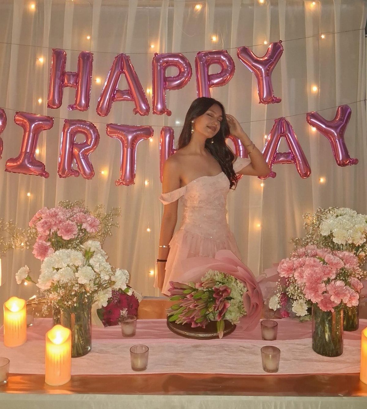 Young woman in a pink A-line dress posing before birthday balloons and flowers