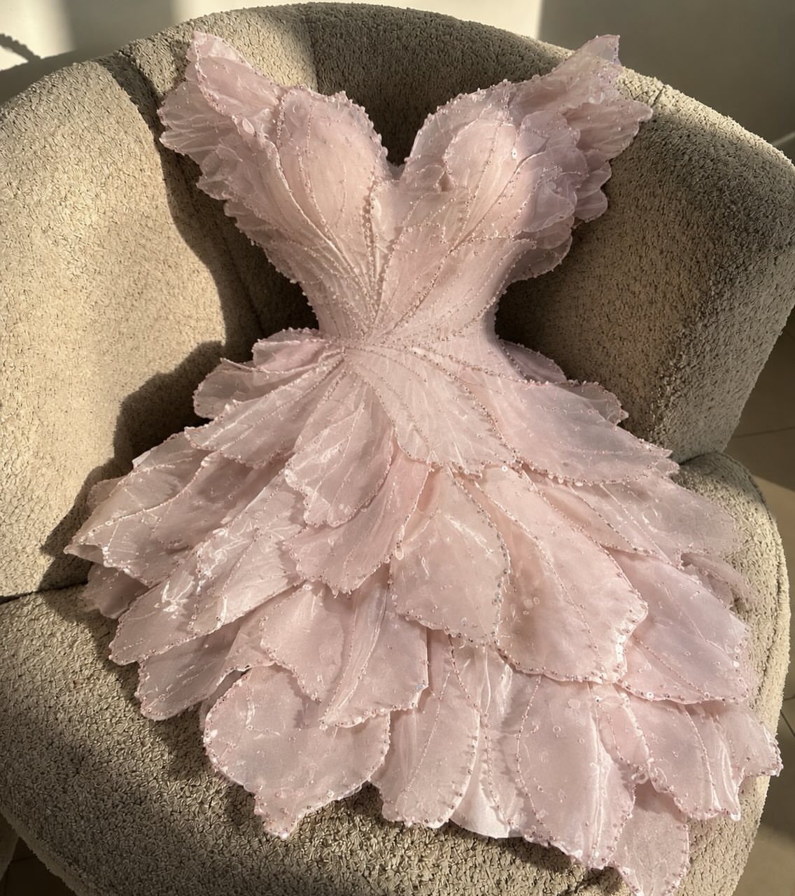 Light pink short dress with petal-layered skirt resting on a beige armchair