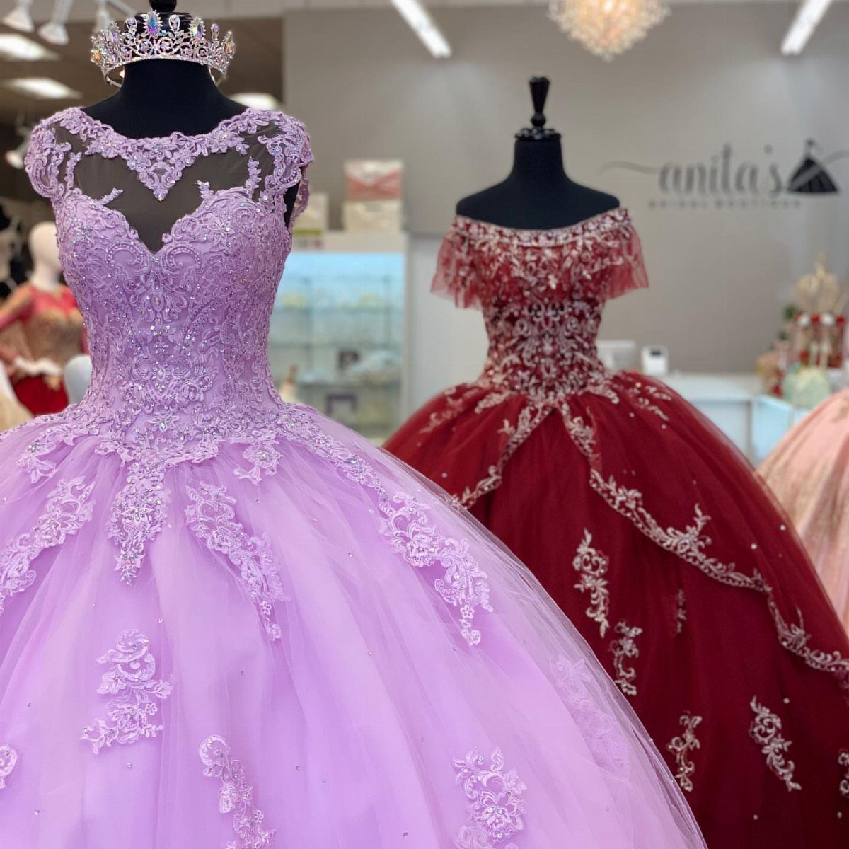 Purple and red ball gowns with lace embroidery displayed on mannequins in a boutique