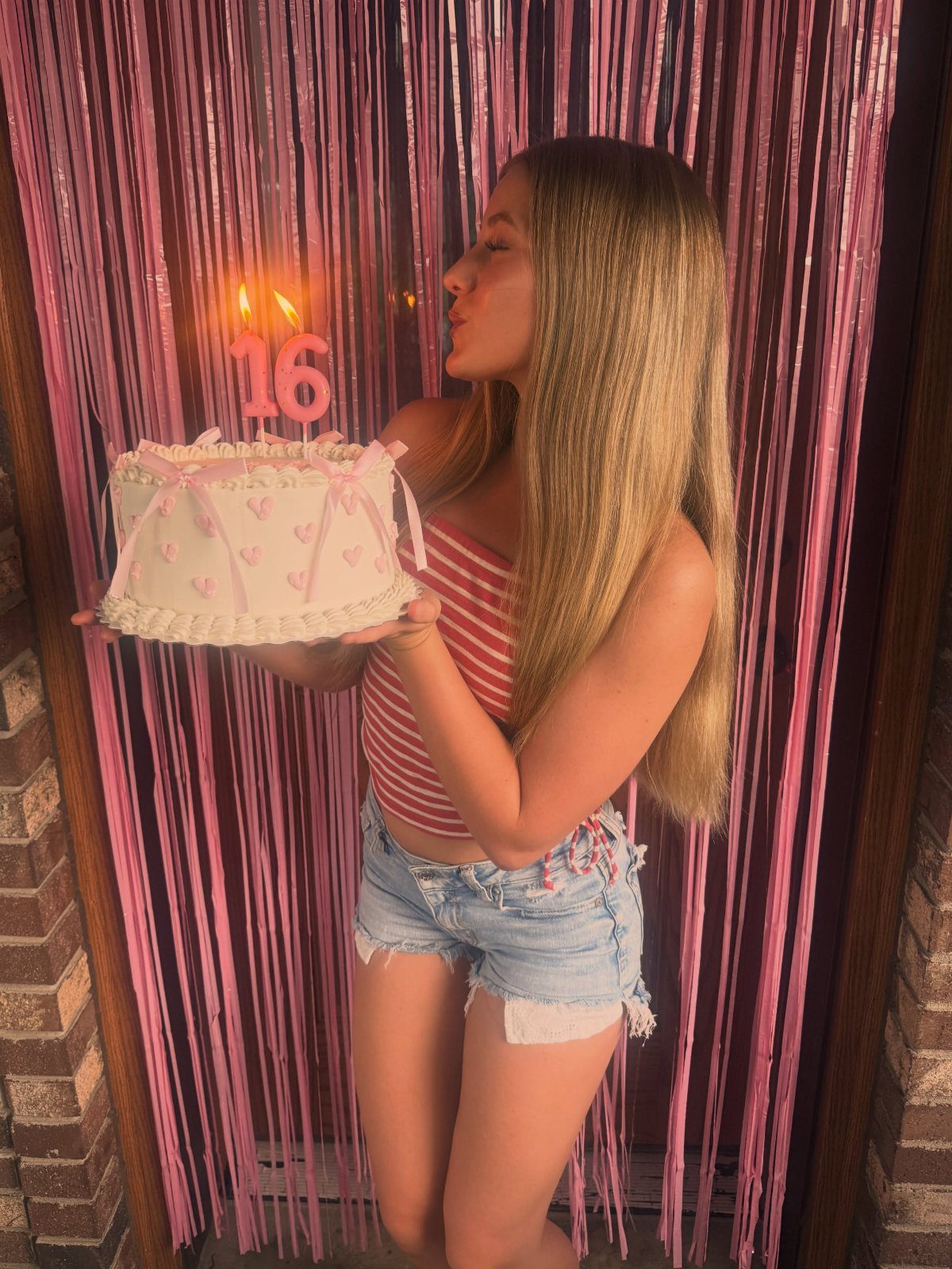 Teenage girl holding a sweet sixteen cake wearing a striped top and denim shorts