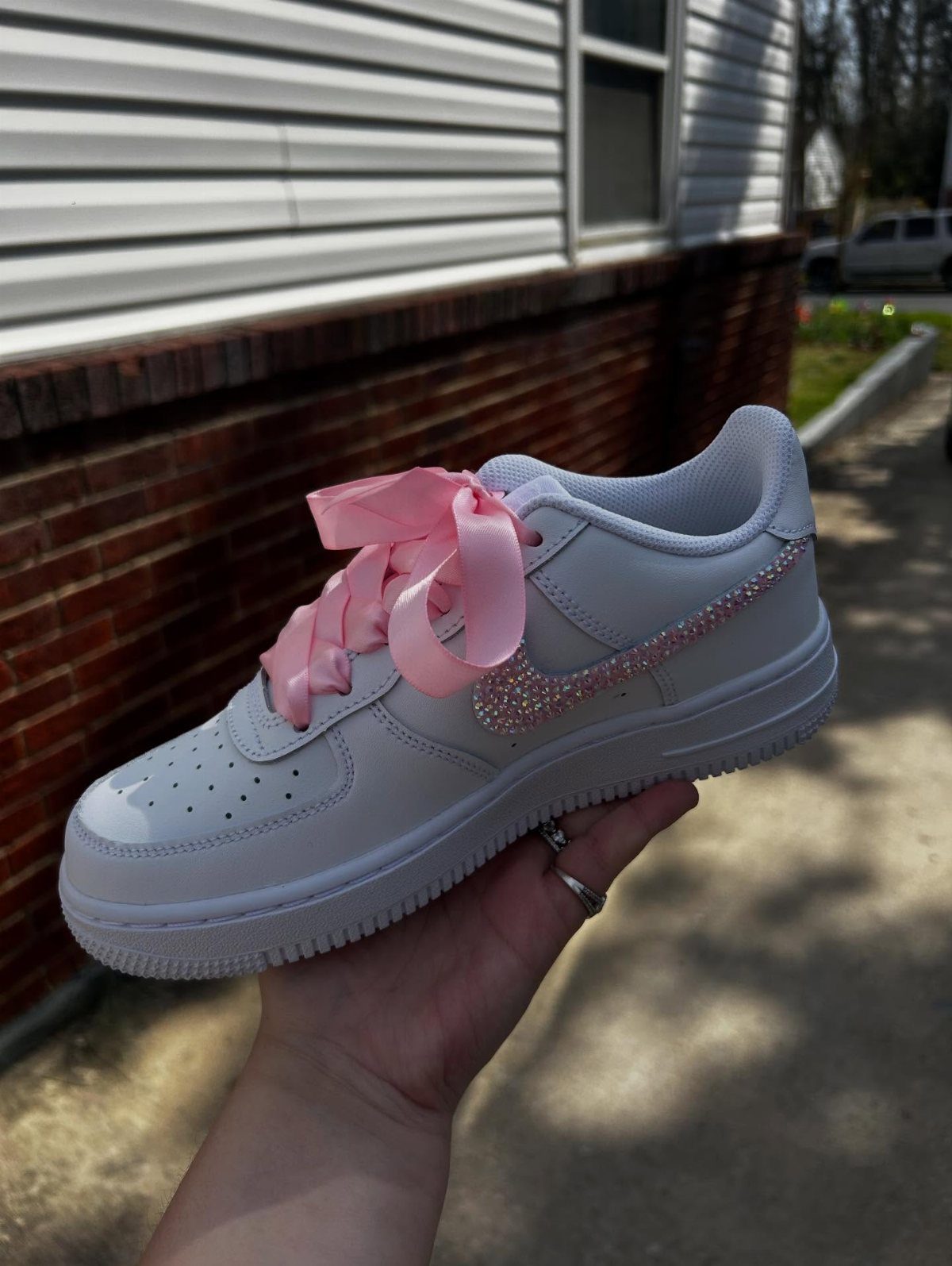 White Nike sneaker with pink rhinestone swoosh and pink satin ribbon laces.