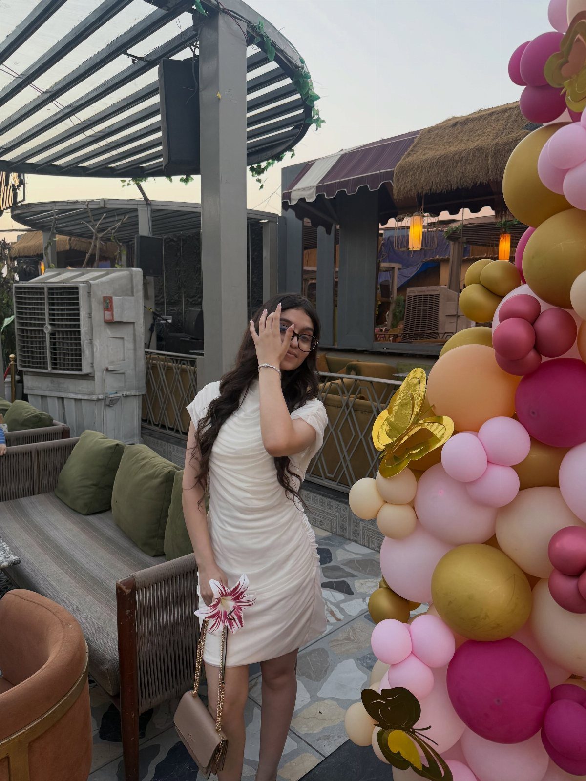 Young woman in a short white dress posing by a colorful balloon arch.