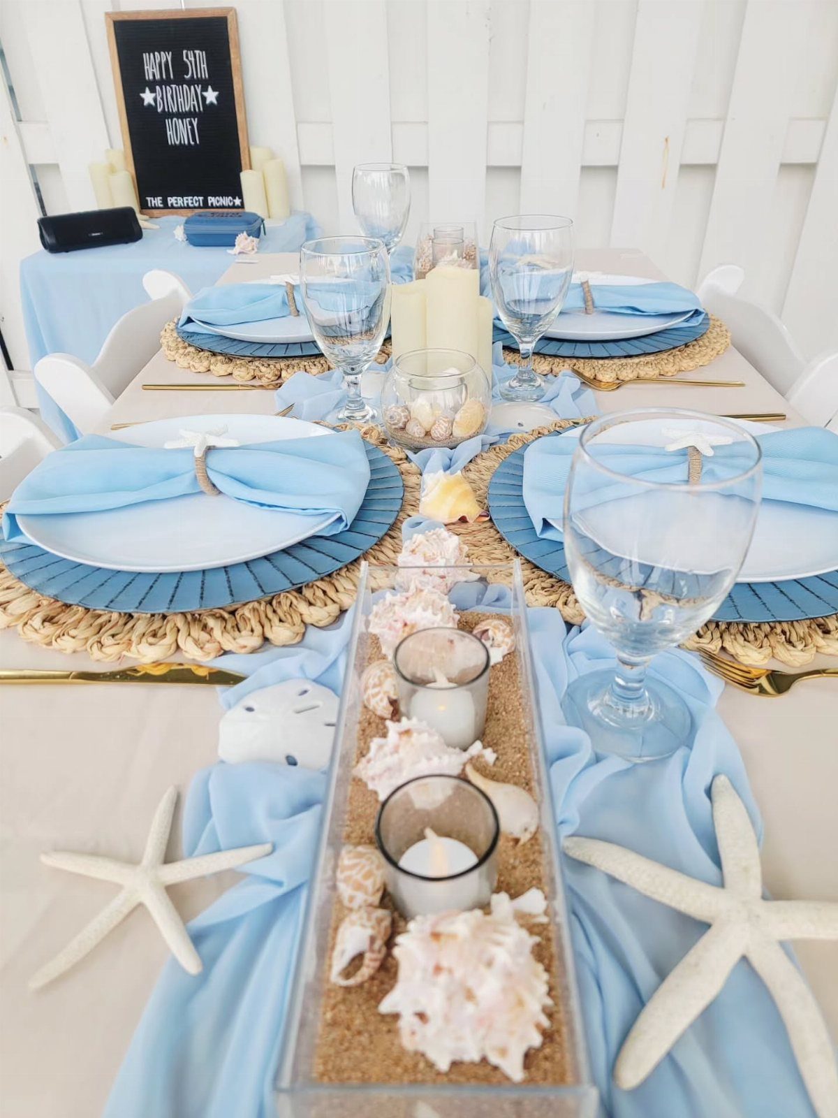 Beach themed table centerpiece with sand, shells, and candles in a glass tray.