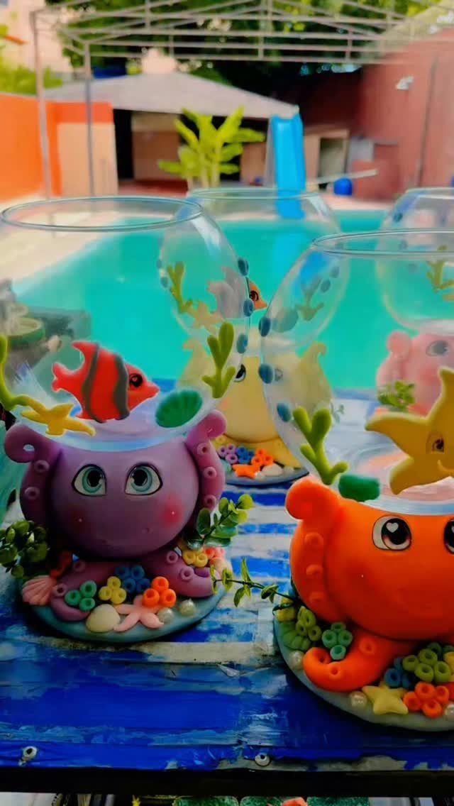 Glass fishbowls with colorful sea creature figures on a blue wooden table outdoors.