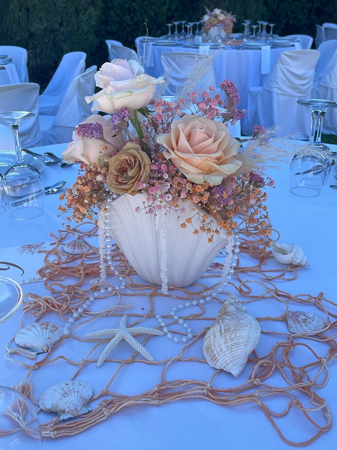 Seashell vase with pink roses on a fishing net with seashells and starfish
