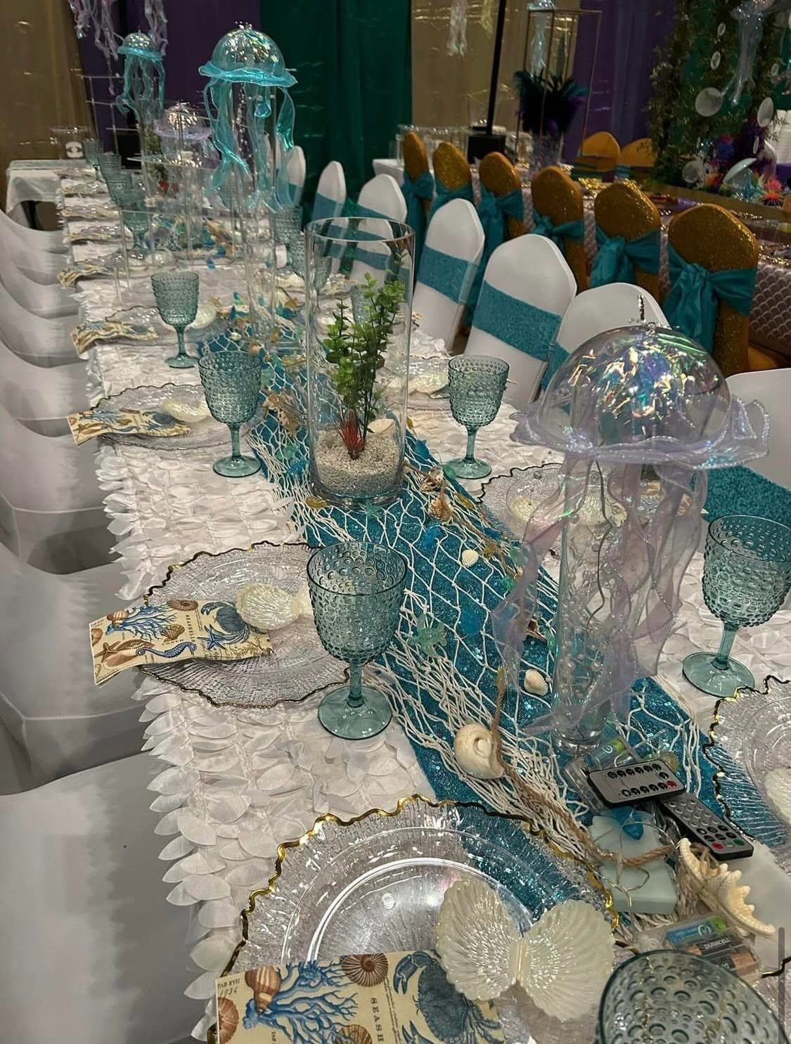 Mermaid themed tablescape with turquoise runner, iridescent jellyfish centerpieces, and blue glassware.