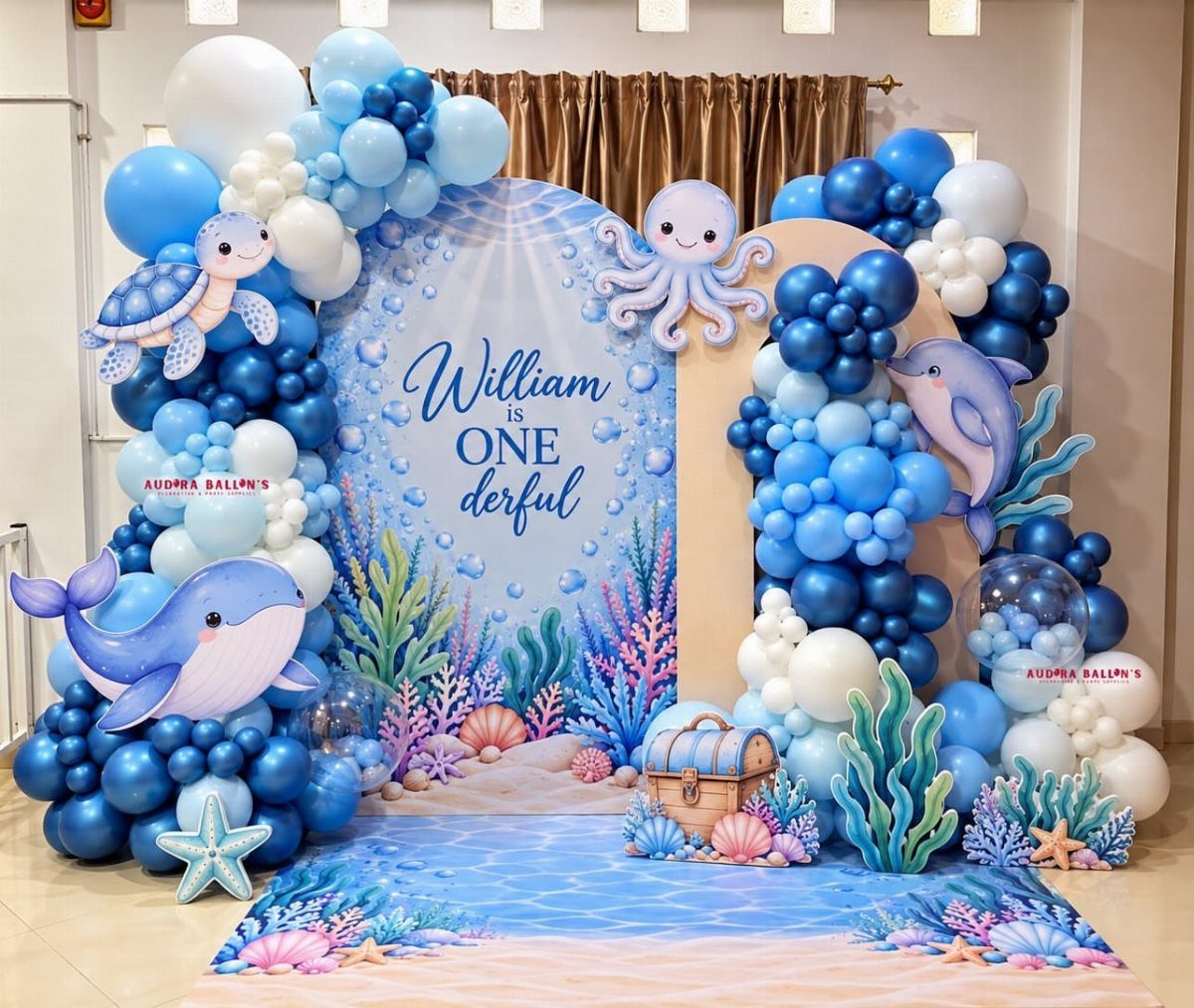 Ocean-themed party backdrop with blue balloons, cartoon sea animals, and a treasure chest.