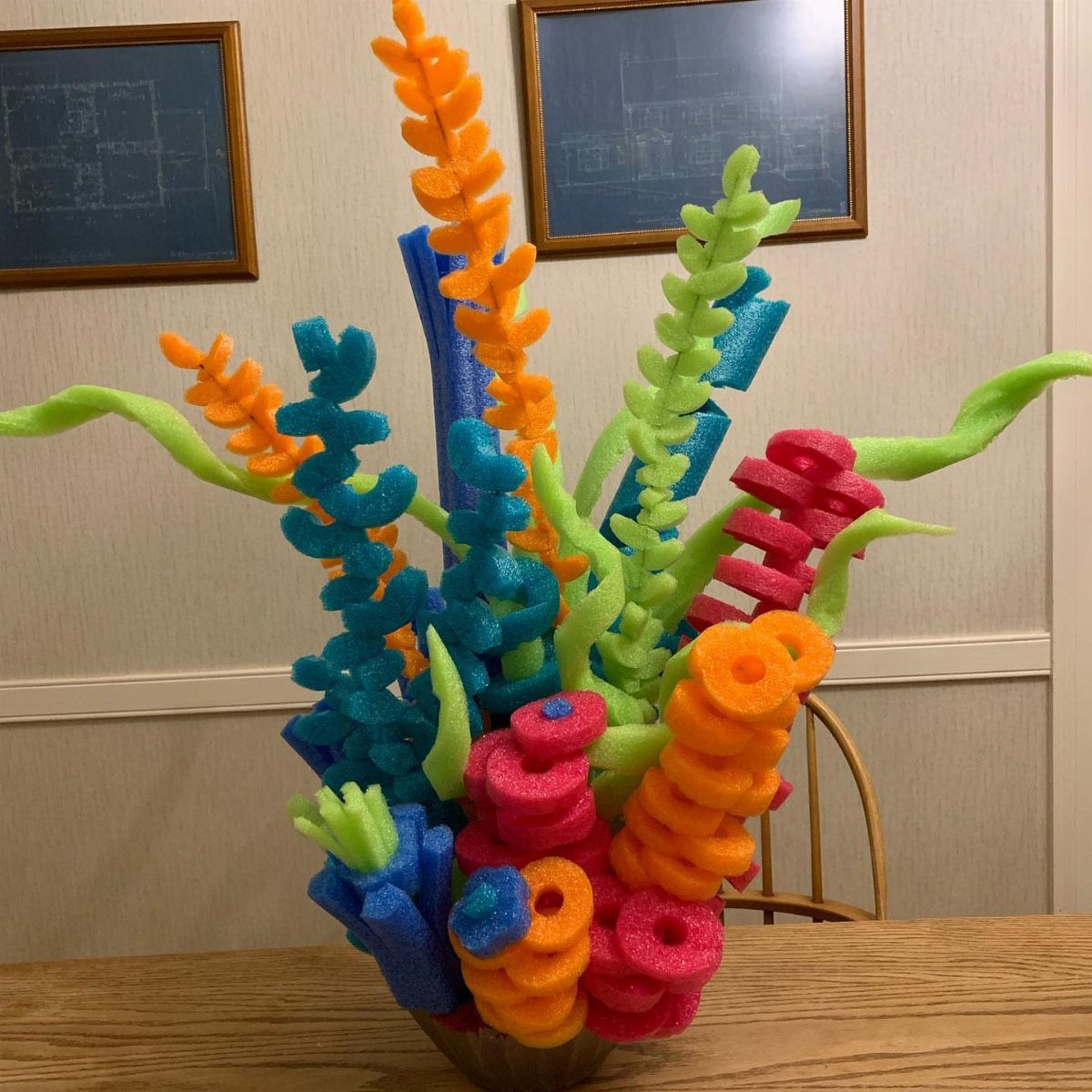Colorful foam pool noodle coral arrangement in a pot on a wooden table.