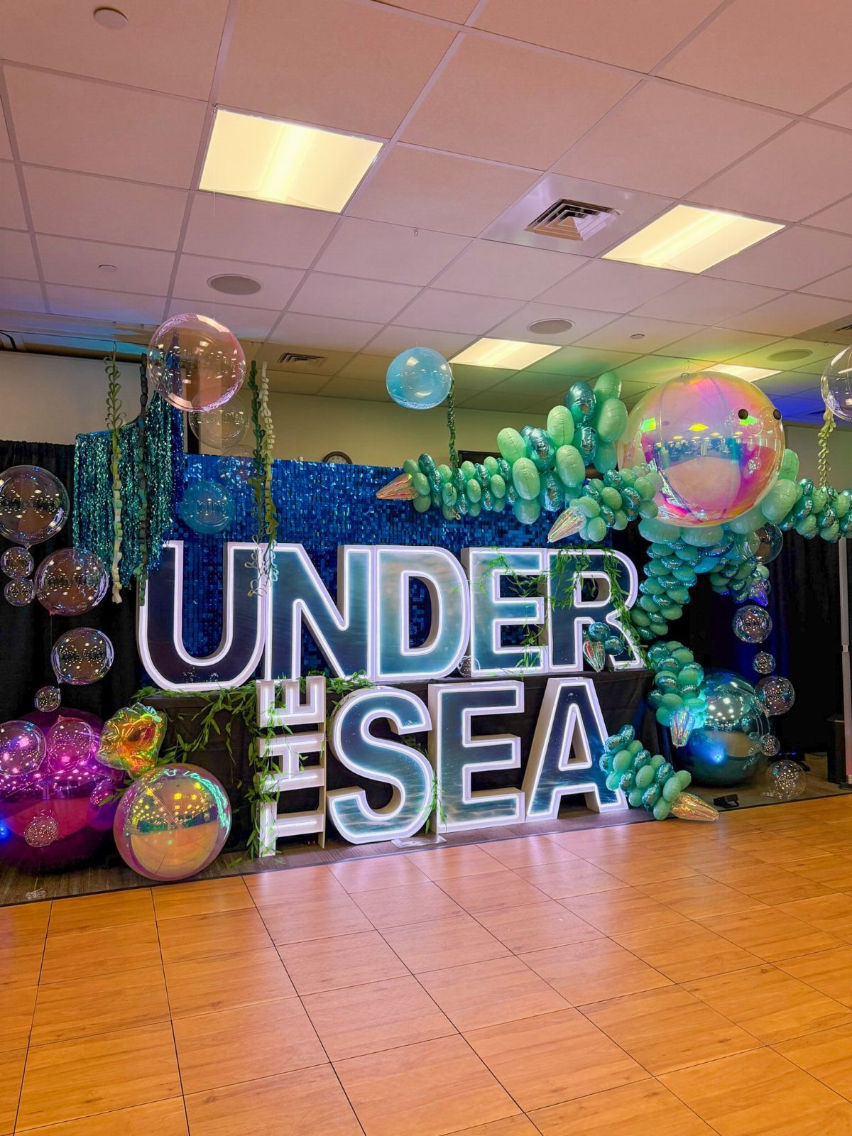 Under the sea event decorations with illuminated letters, blue sequins, and teal balloons.
