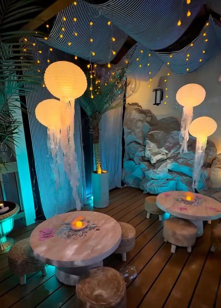 Glowing jellyfish lanterns hanging in a blue themed undersea event space with tables.