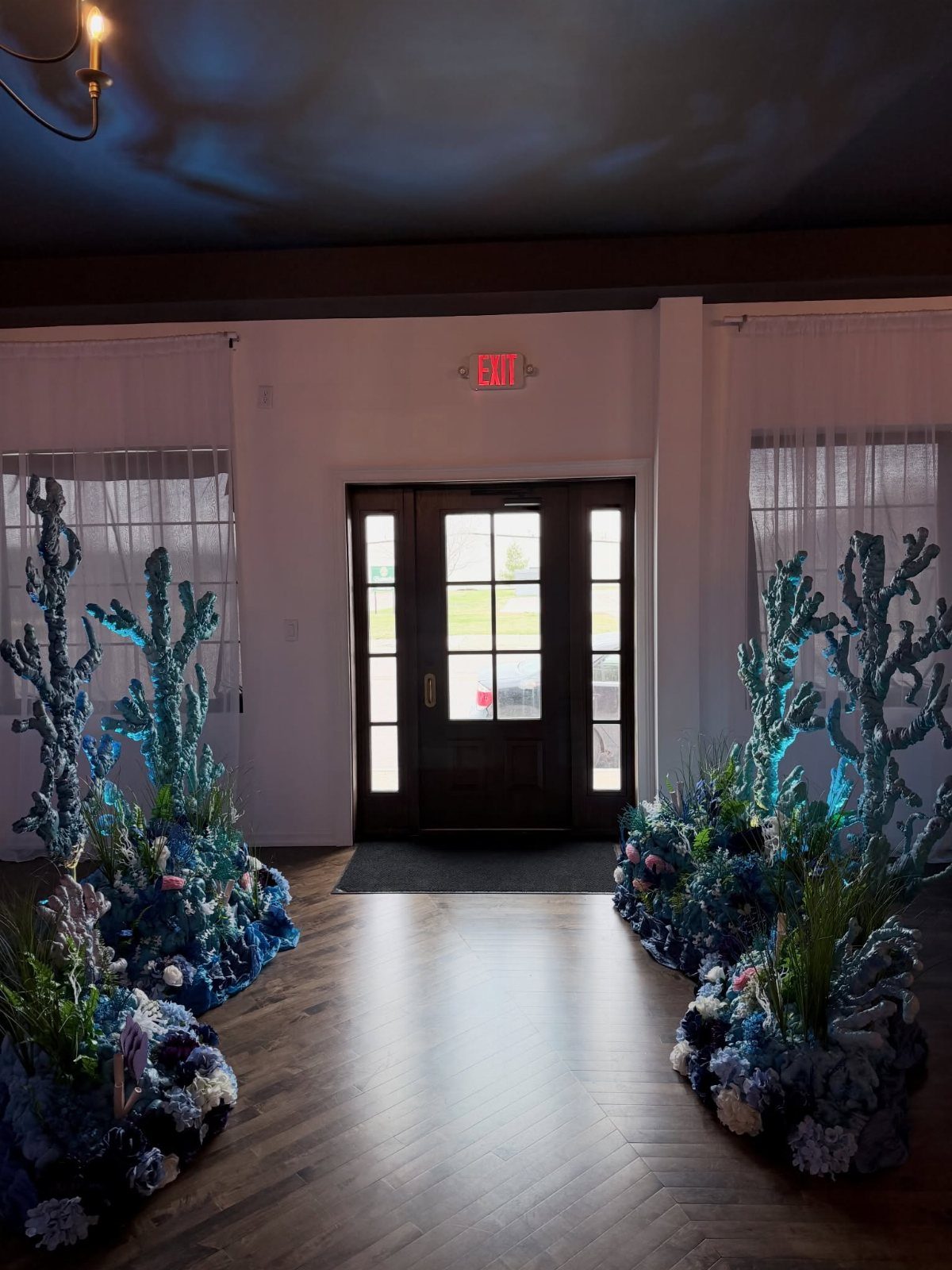Blue coral sculptures and floral arrangements lining a hallway with underwater lighting.