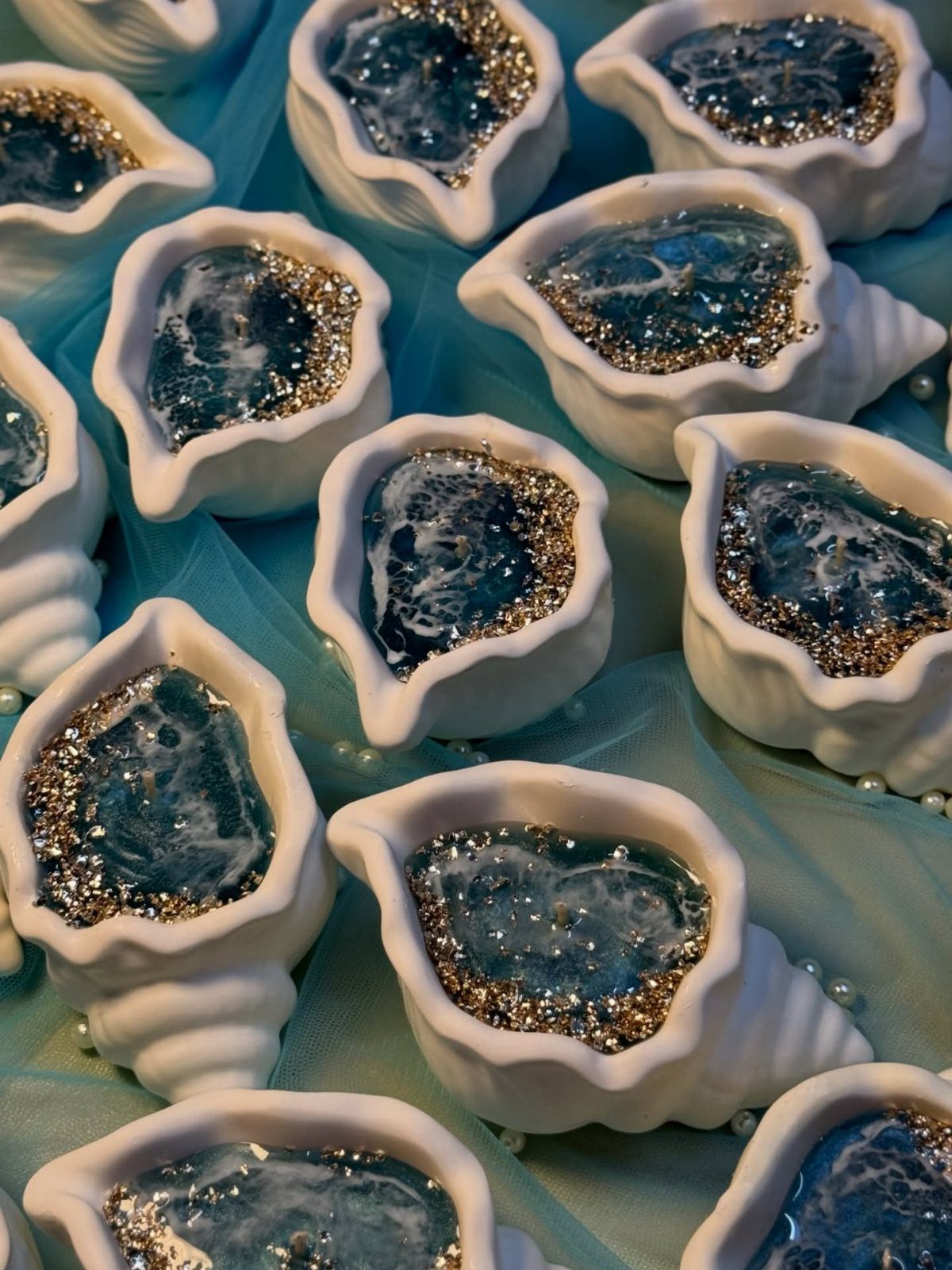 White shell-shaped candle holders filled with blue resin and gold glitter on blue fabric.