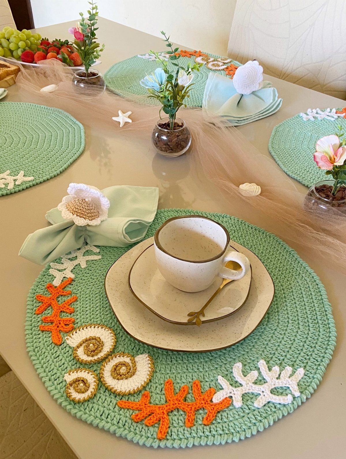 Mint green crochet placemats with coral and shell designs on a decorated table.