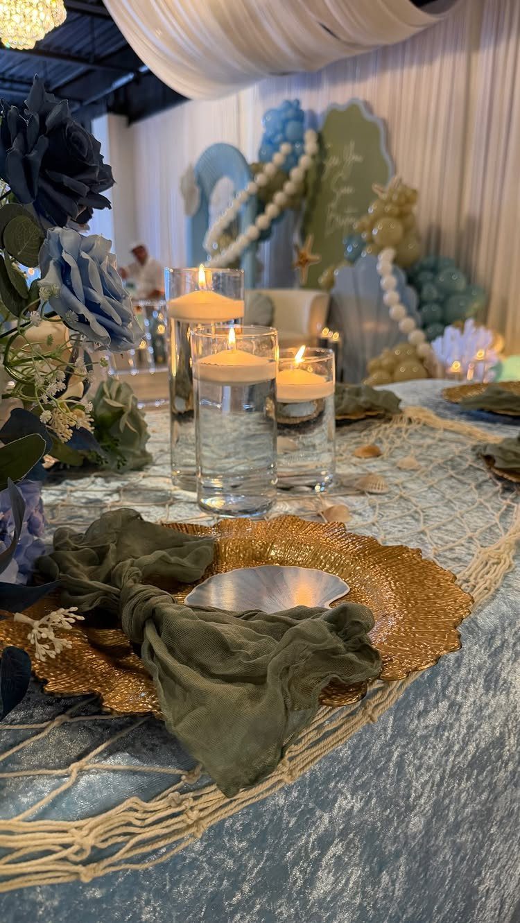 Under the sea wedding table setting with blue cloth, gold plates, and floating candles.