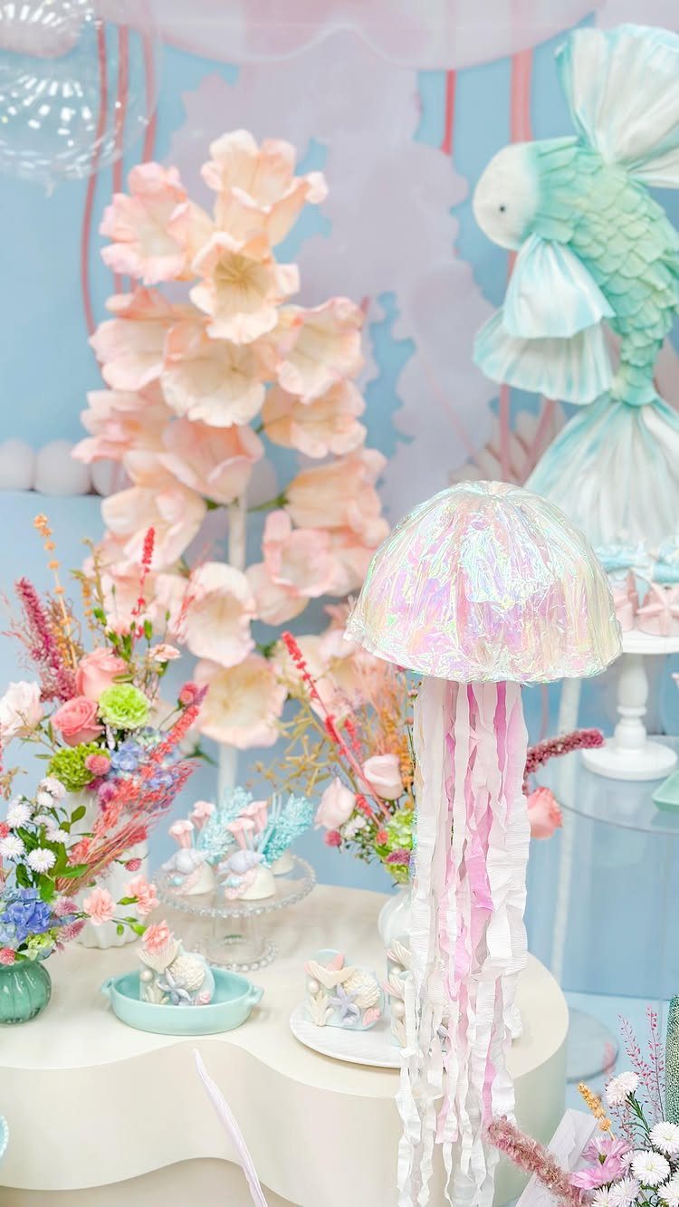 Pastel under the sea themed dessert table with jellyfish and fish sculptures.