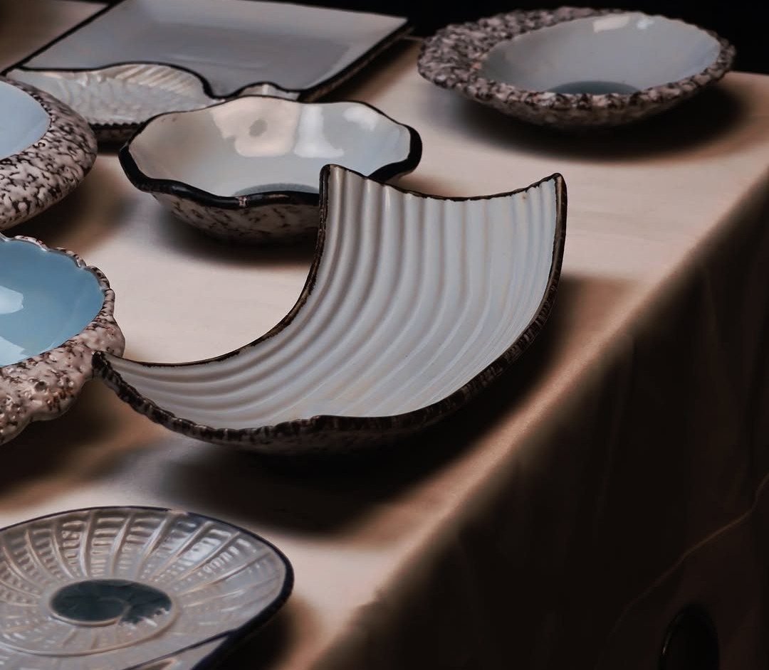 Organic ceramic bowls and plates in blue and white on a beige tablecloth.