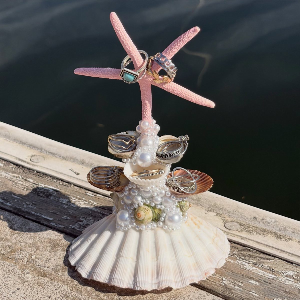 Pink starfish and seashell ring holder with wedding bands on a wooden dock