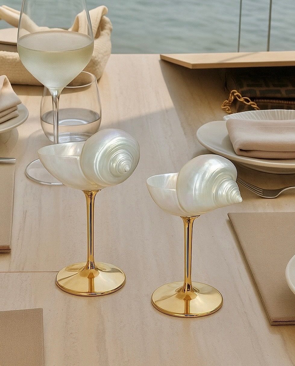 Shell-shaped iridescent glasses with gold stems on a set dining table by the water