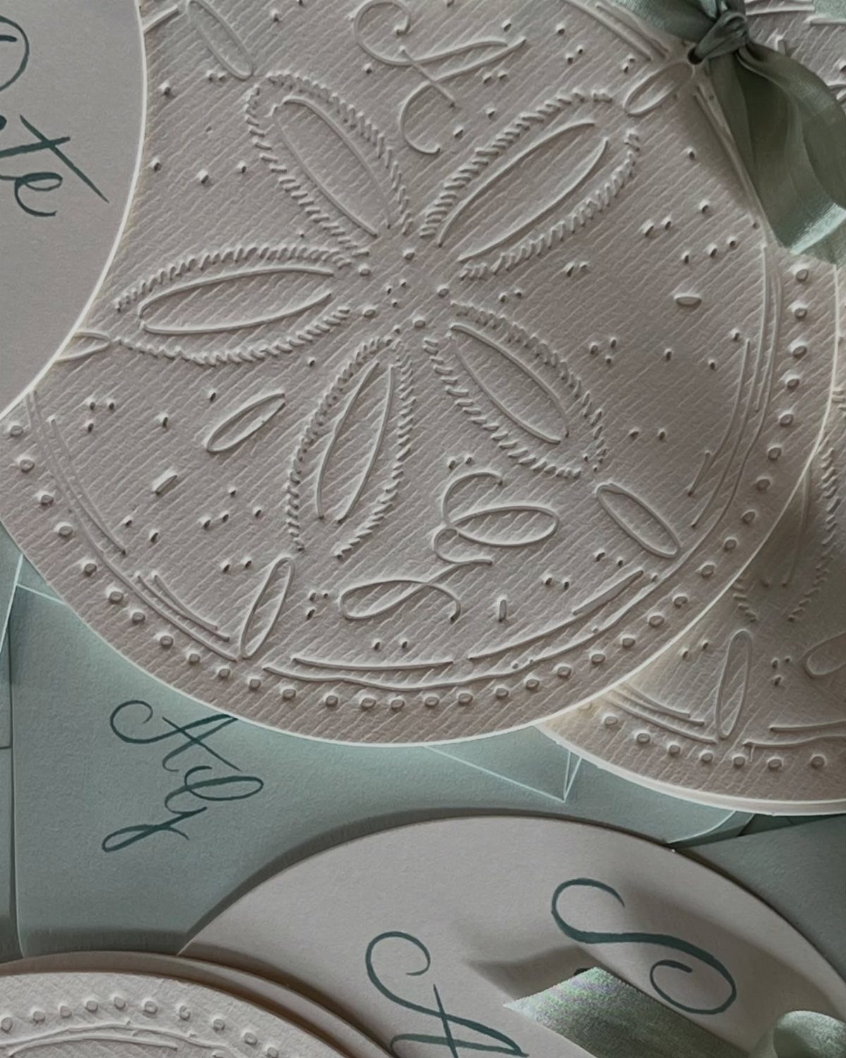 Embossed white wedding invitations with seashell patterns and mint green ribbons and envelopes.