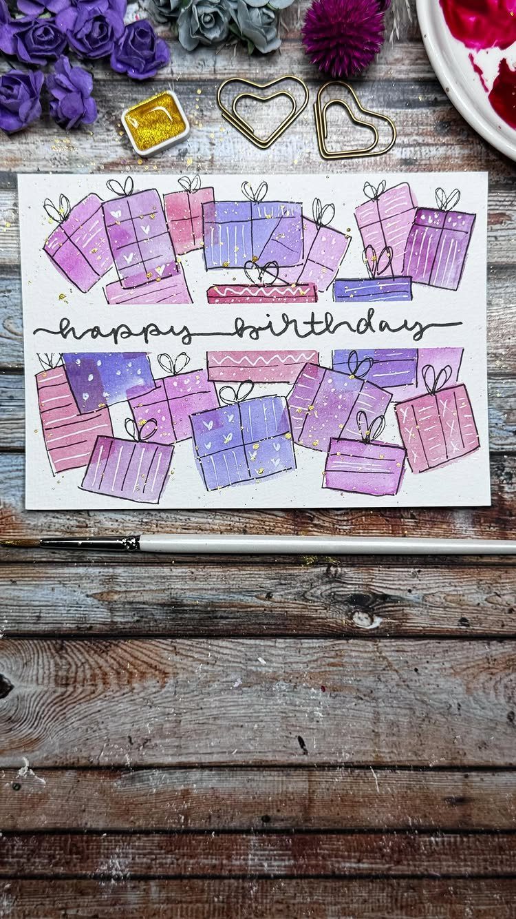 Handmade birthday card with watercolor gift boxes and gold glitter accents on wood.