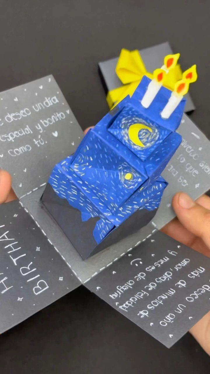 Pop-up birthday card with a blue starry cake and yellow candles held by hands.