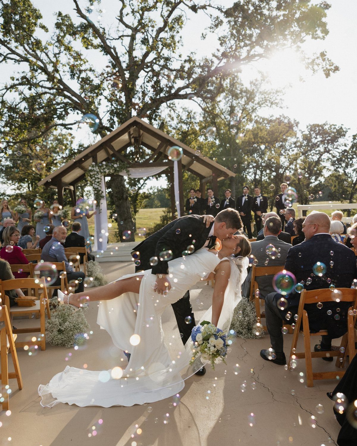 Bride and groom kissing in a dip surrounded by floating bubbles at wedding
