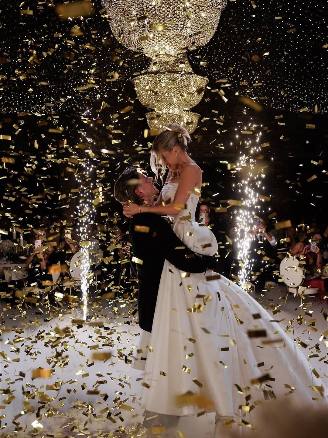 Bride and groom embracing on a dance floor surrounded by falling gold confetti.