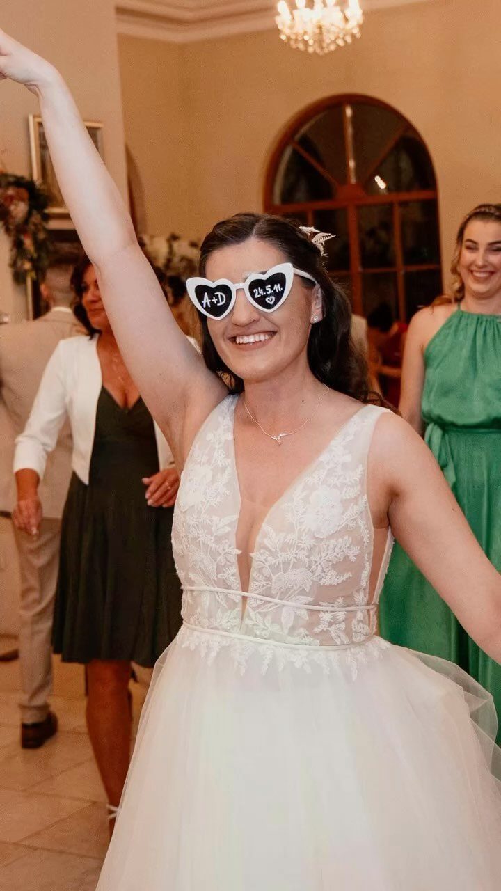 Bride in white wedding dress wearing heart-shaped sunglasses and smiling at a party