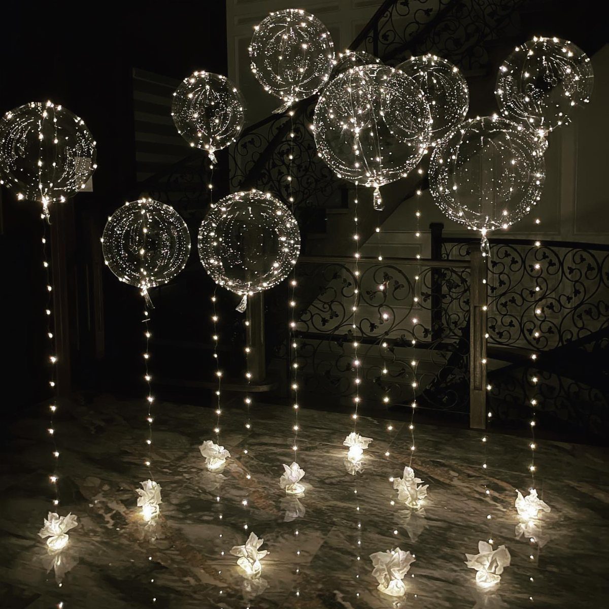 Clear LED balloons with fairy lights floating over a dark marble floor