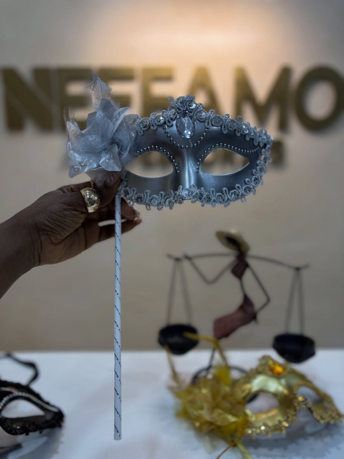 Silver masquerade mask on a stick held by a hand against a blurred background