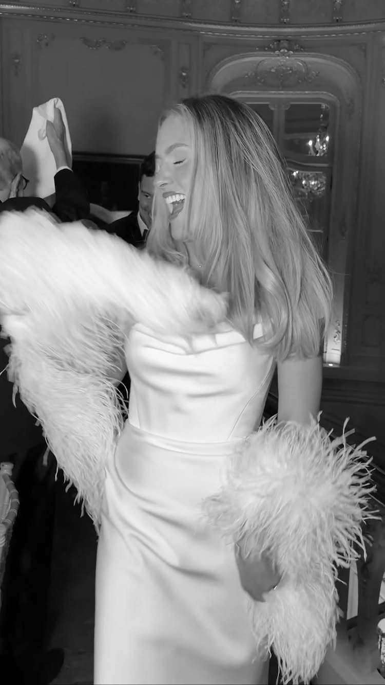Woman in white dress dancing and laughing while wearing a white feather boa.