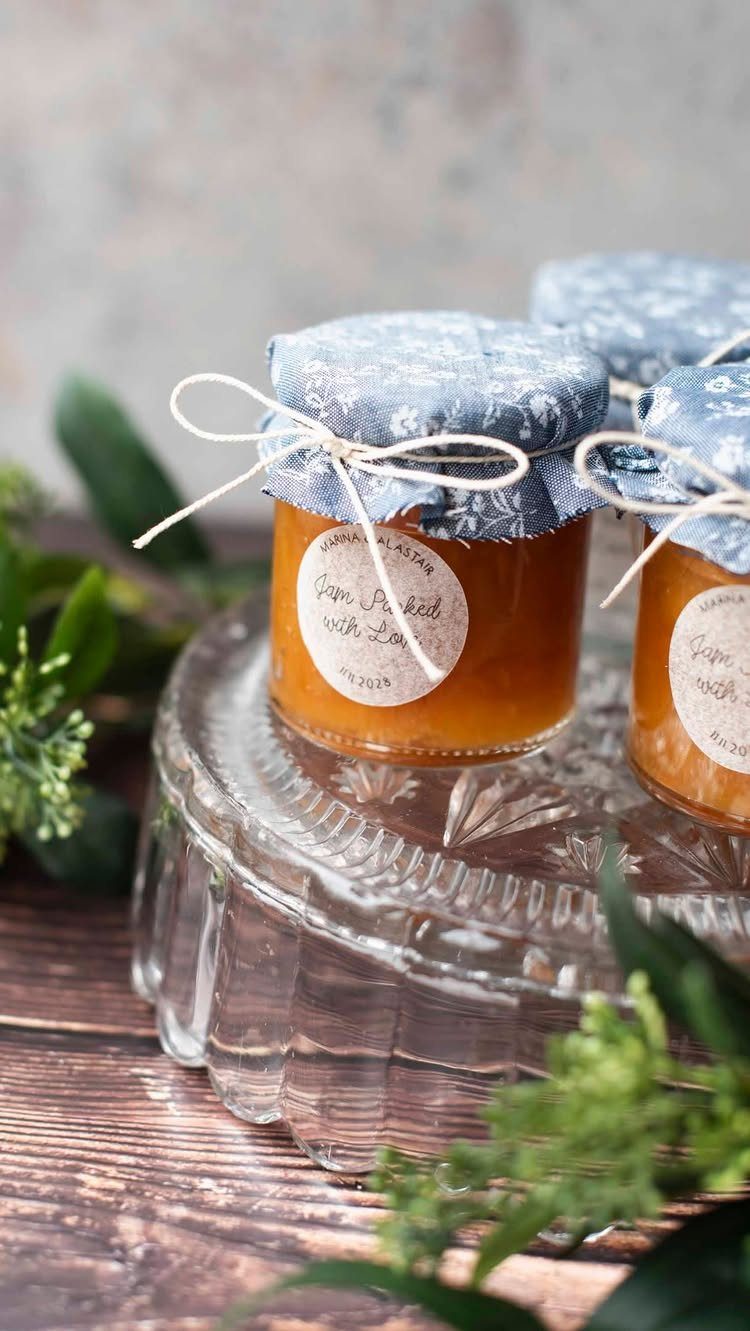 Small jars of orange jam with blue fabric lids and personalized white labels.