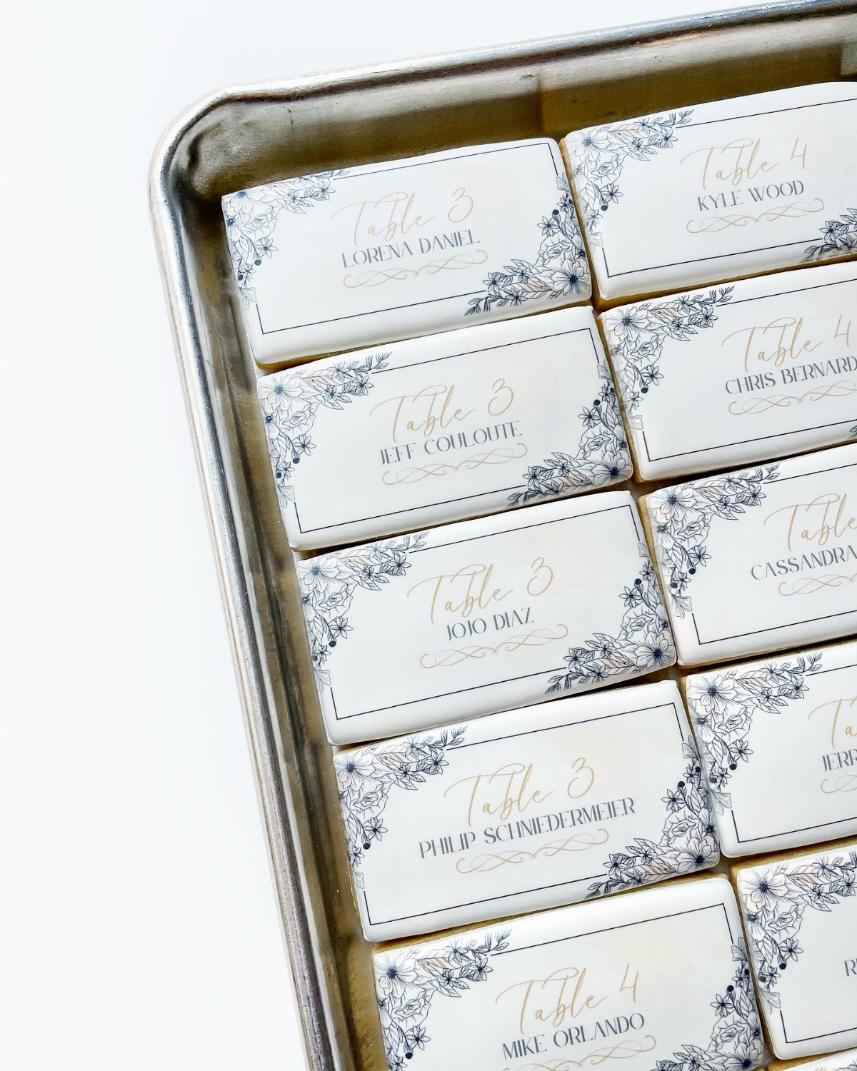 White iced cookies with guest names and table numbers on a silver tray.