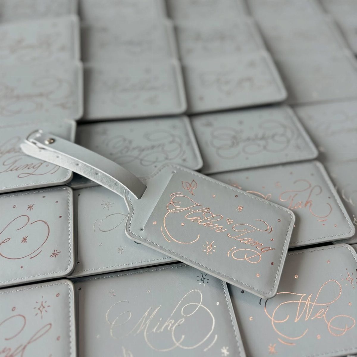 Light grey leather luggage tags with rose gold engraved names in cursive script.