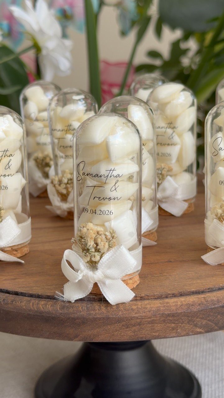 Small glass vials filled with white candies and dried flowers on wooden stand.