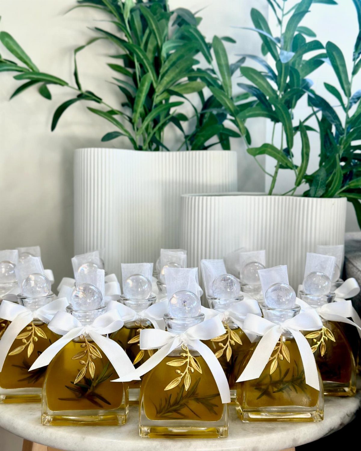 Small square glass bottles of infused olive oil with white ribbons and gold leaves.