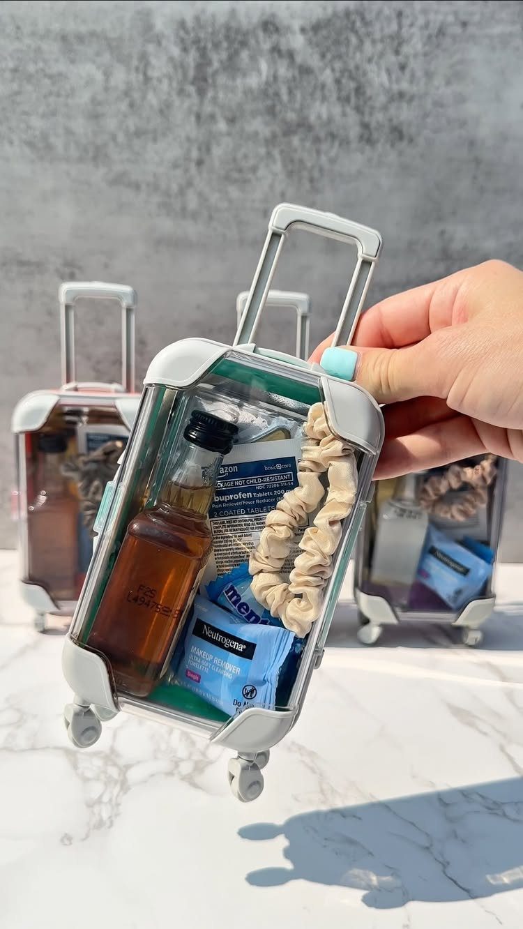 Miniature suitcase containers filled with a small bottle, packet, and hair scrunchie.