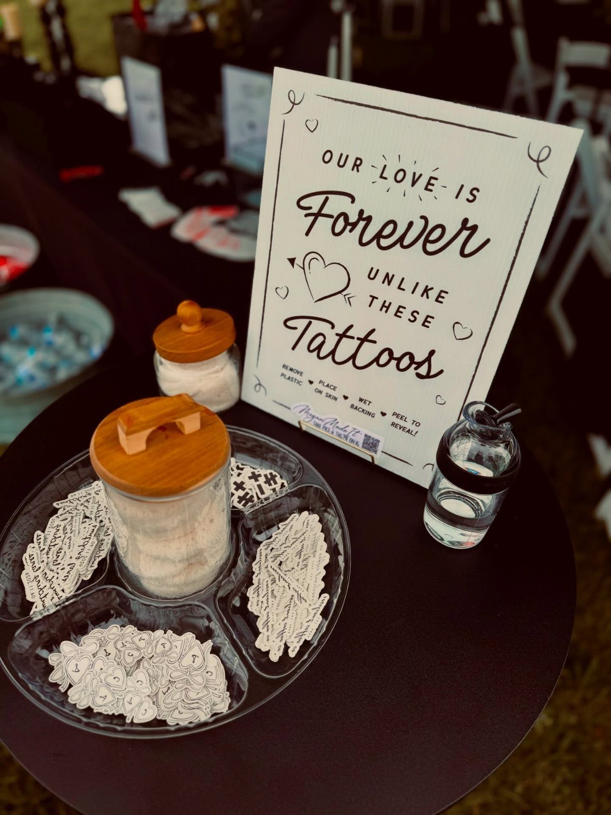 Temporary tattoos in a glass tray next to a wedding sign on a table.