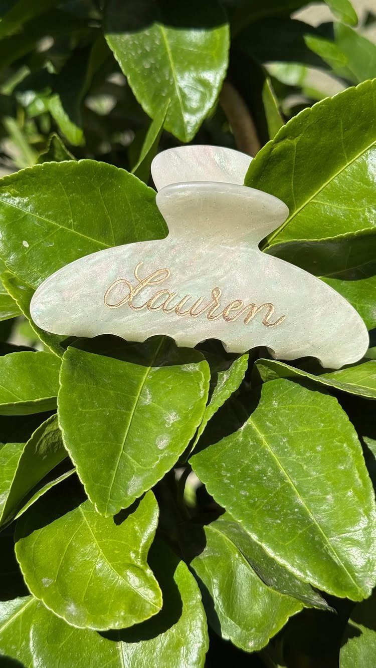 White pearlescent hair claw clip with gold name Lauren on green leaves