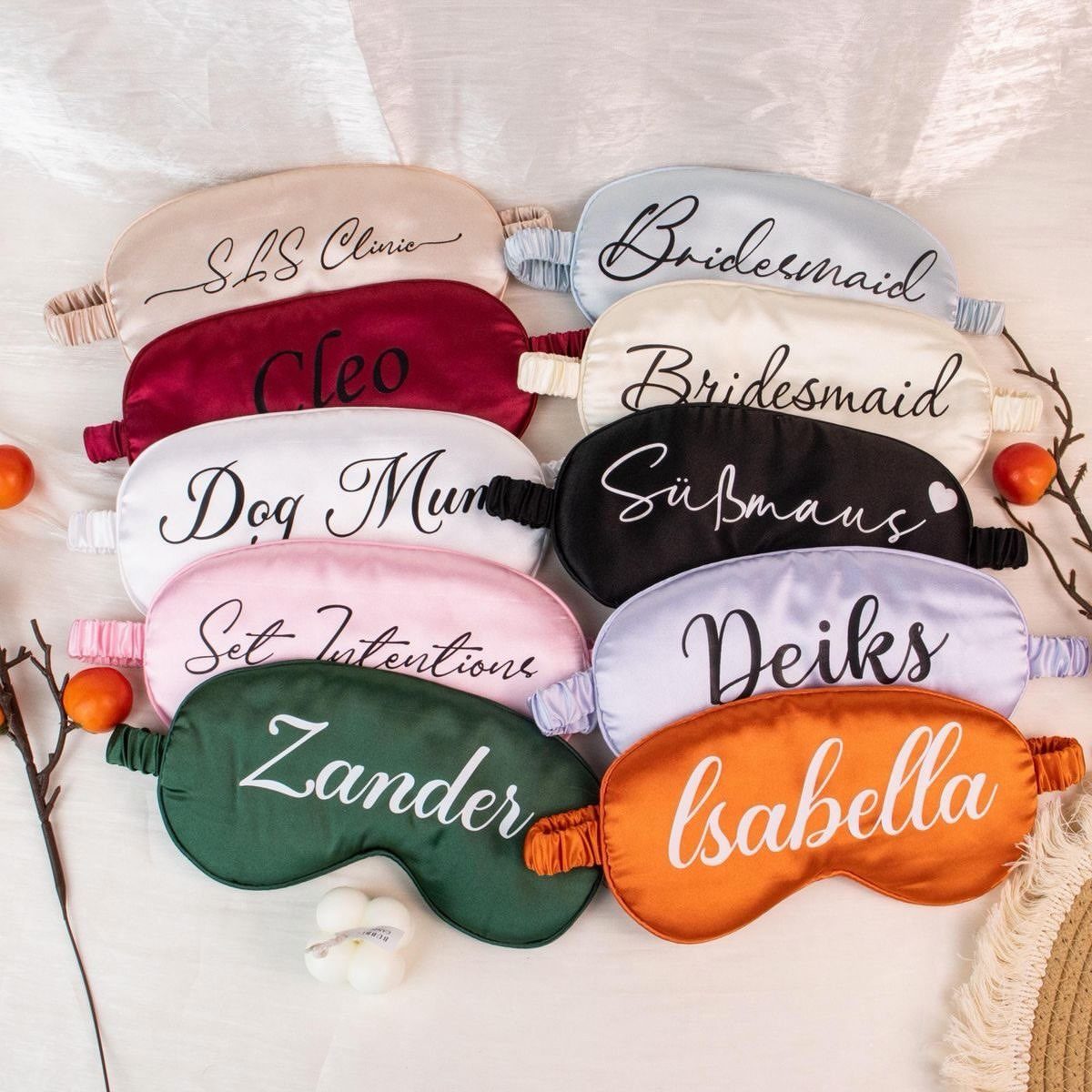 Personalized satin sleep masks in multiple colors arranged on a white fabric background.