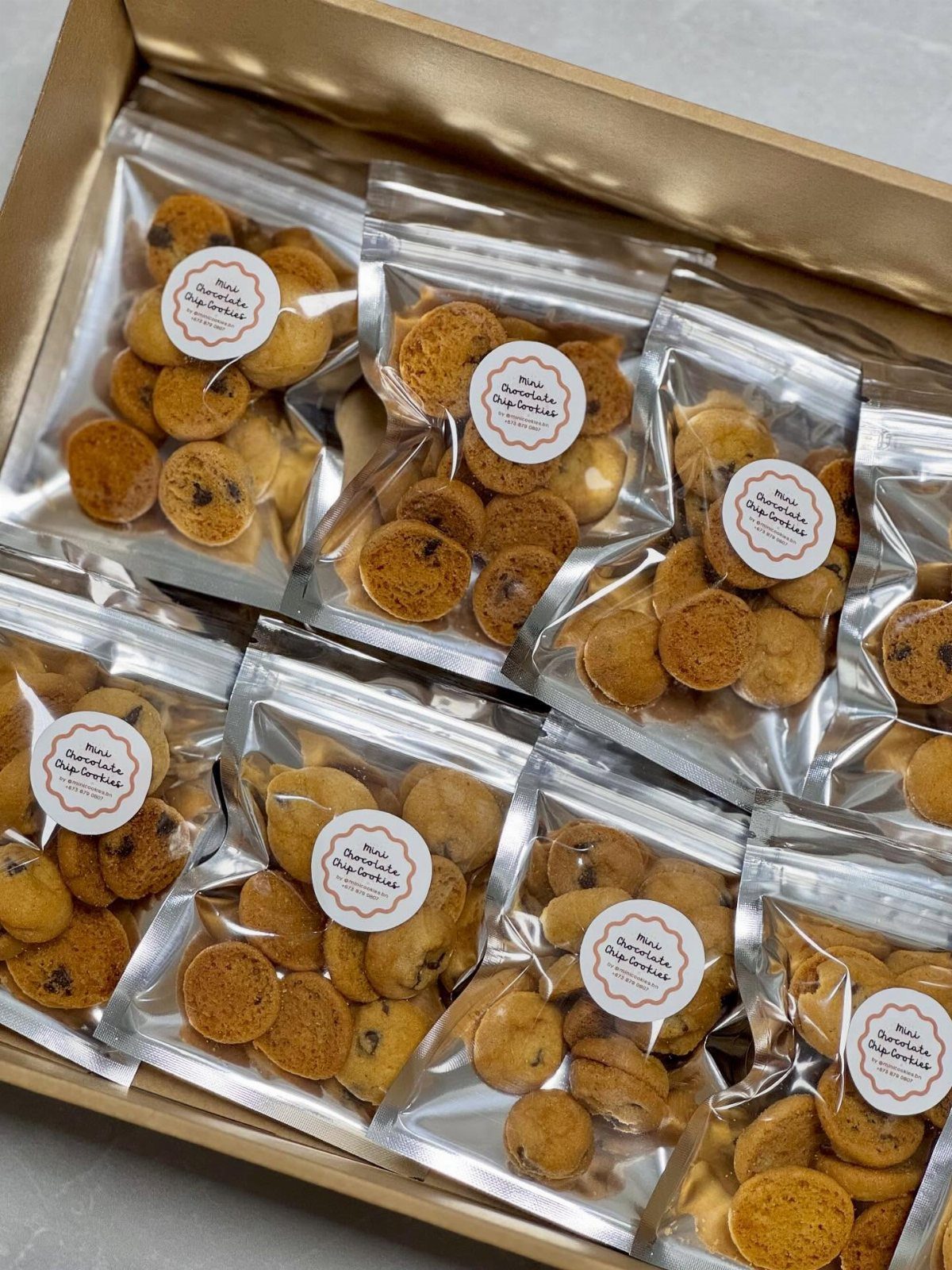 Mini chocolate chip cookies in clear bags with labels inside a gold box.