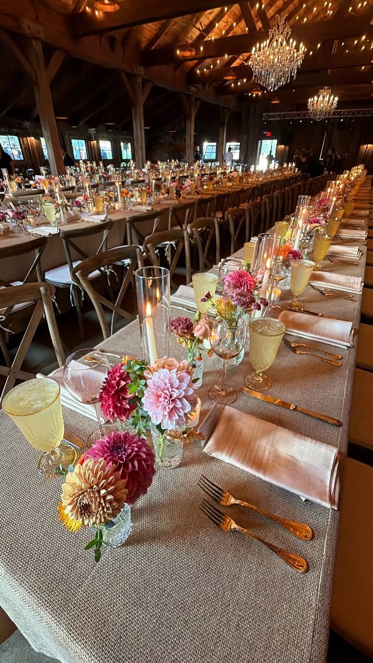 Long reception table with colorful dahlia blooms in small glass bud vases and candles.